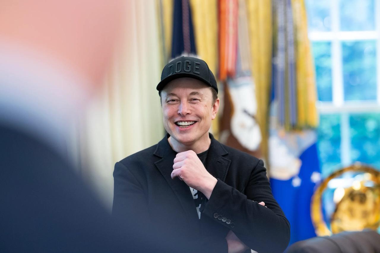 Elon Musk at a White House event, smiling with a hat on.